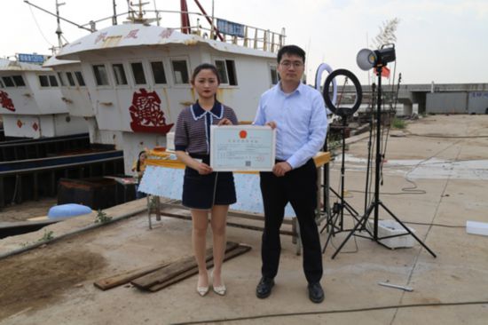 海鮮電商張夢(mèng)琴與幫辦員手持食品經(jīng)營許可證合影。贛榆區(qū)委宣傳部供圖